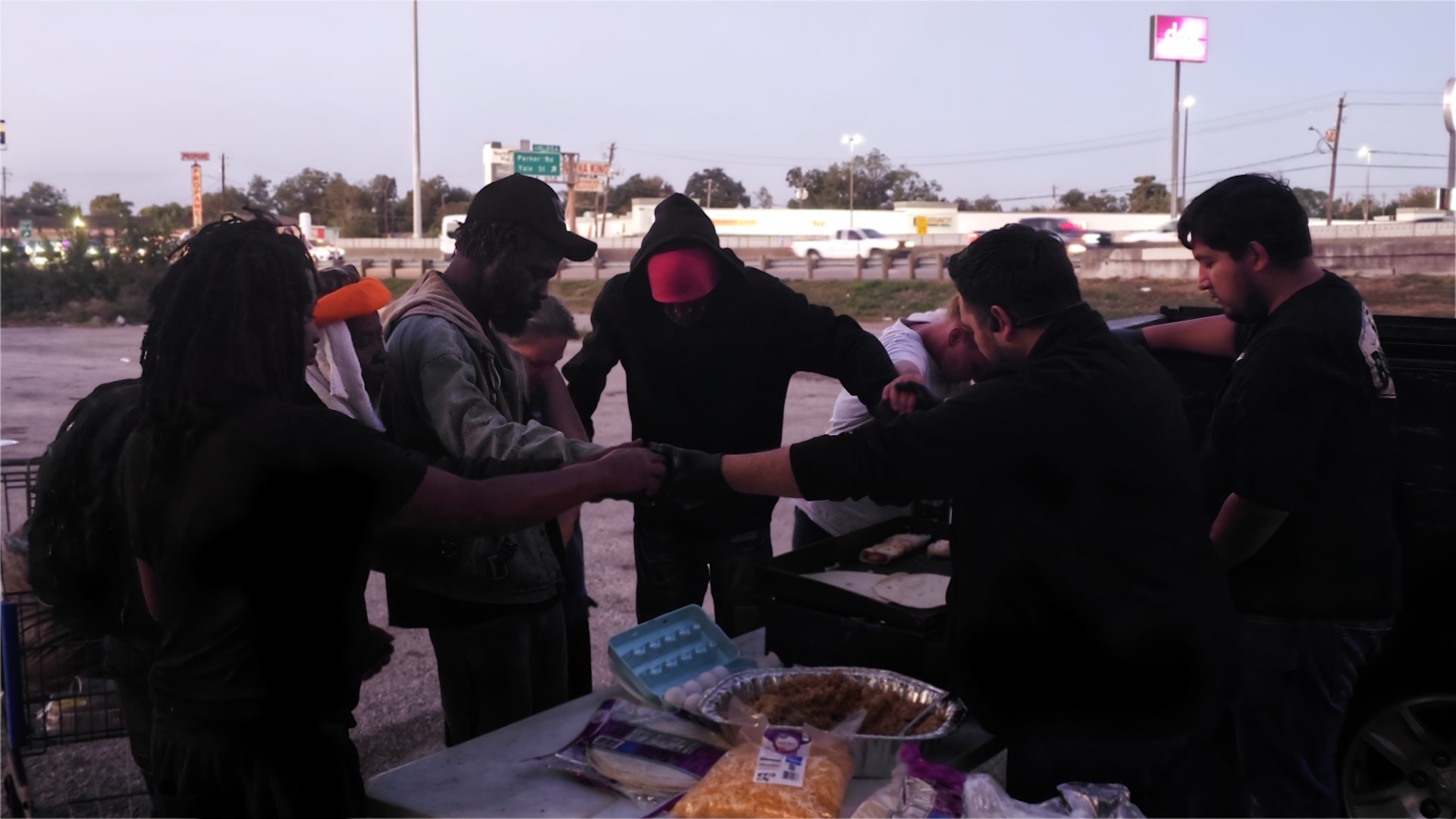 A group joining hands in prayer during a JC Lives food outreach