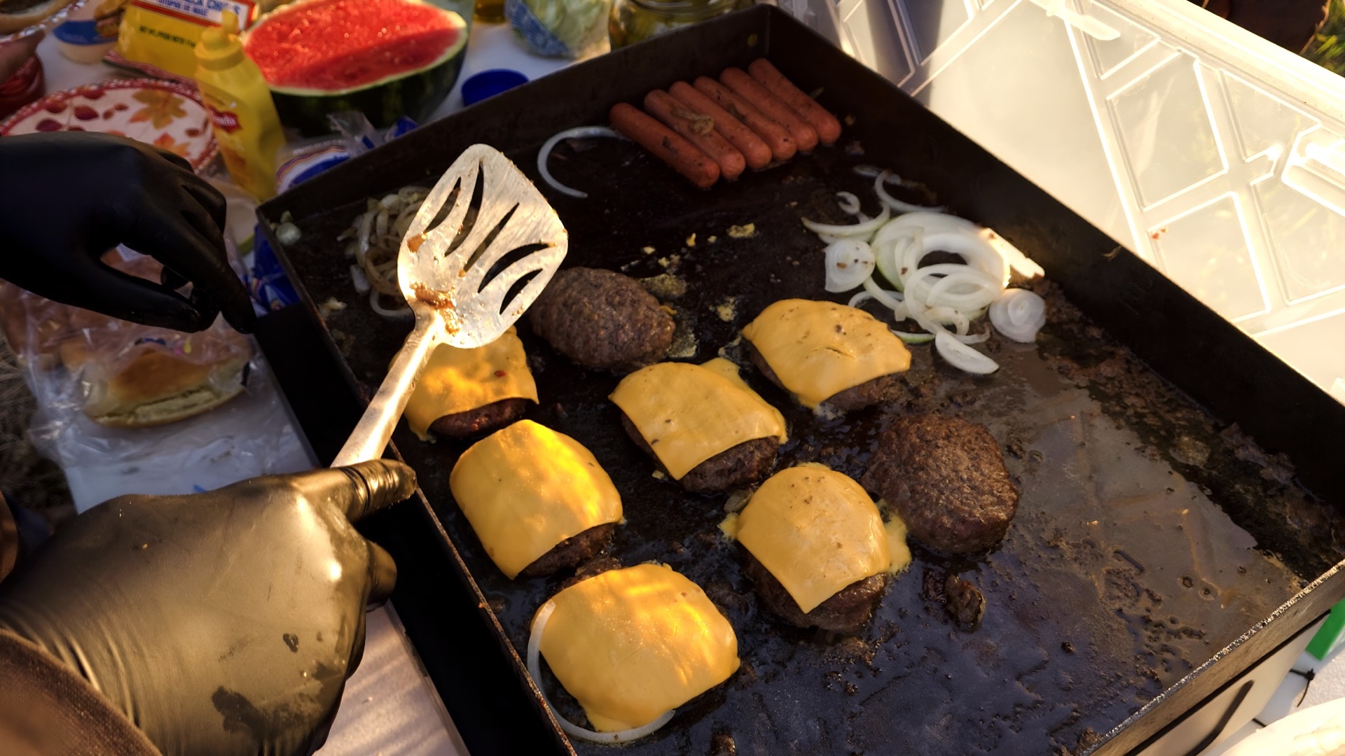 Burgers, hot dogs, and onions cooking on the outreach griddle